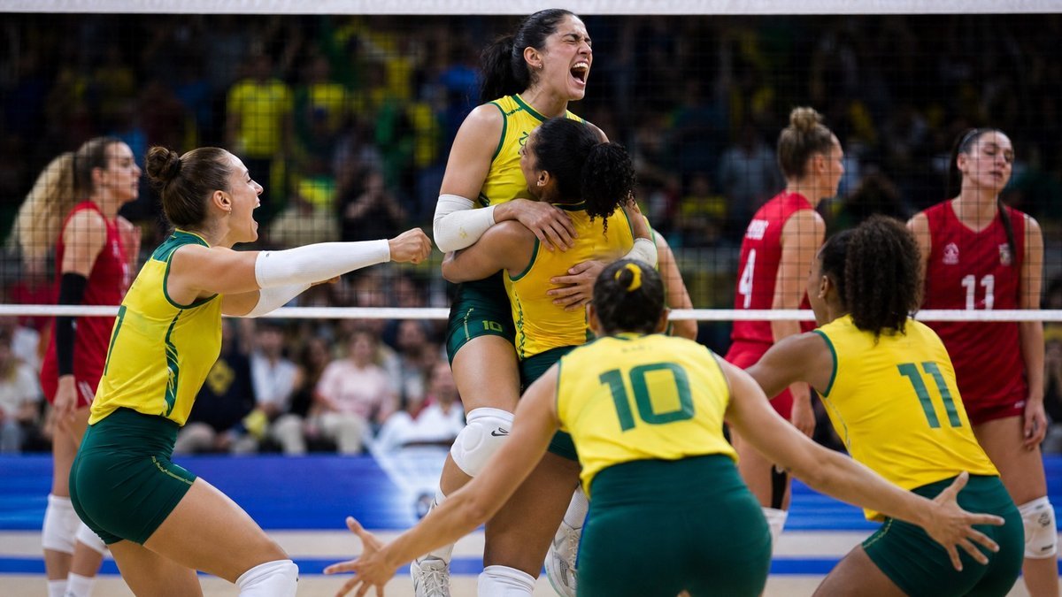 Jogadoras de vôlei celebram ponto decisivo em quadra coberta durante partida internacional.